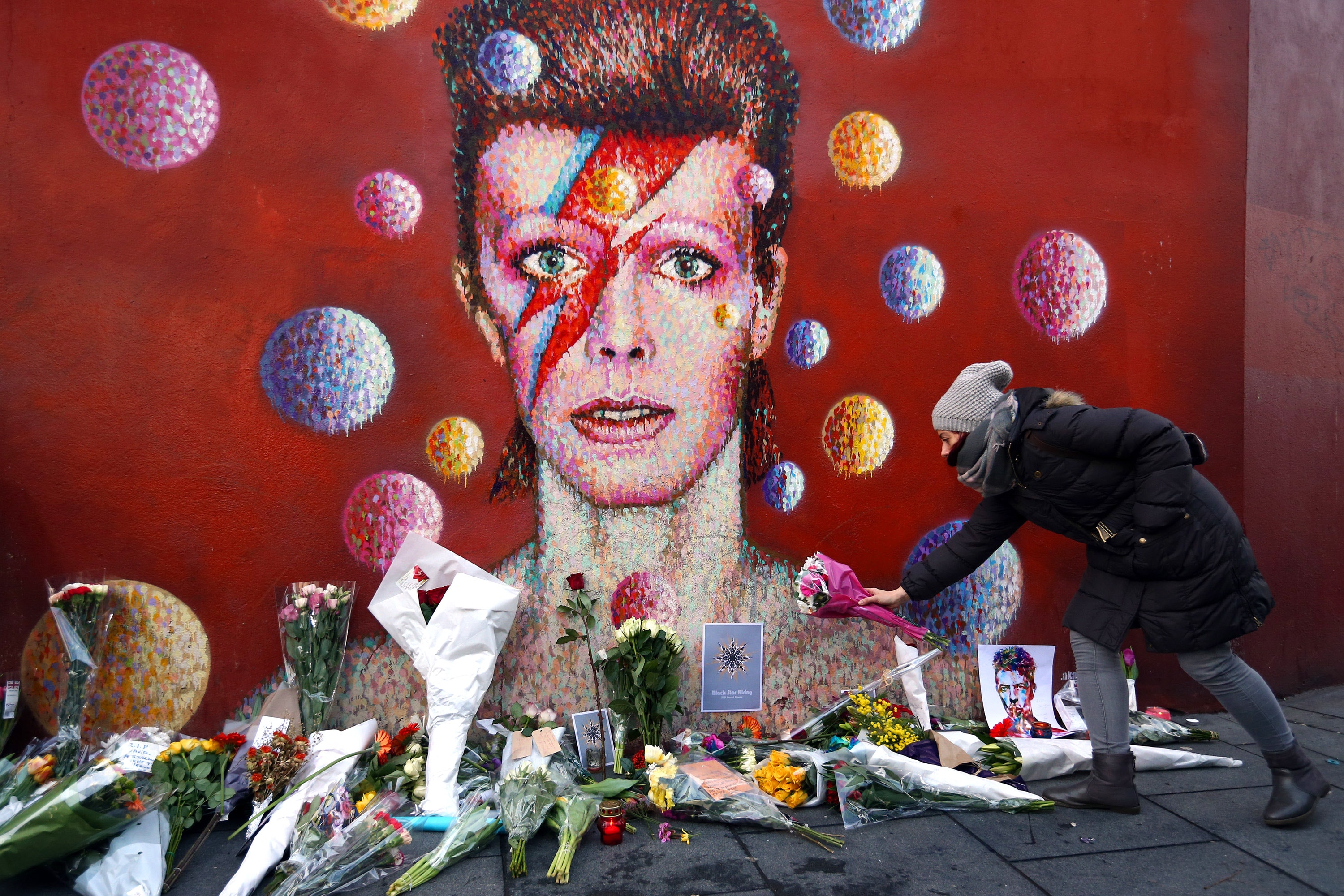 Londra, 11 gennaio 2016. Una donna lascia dei fiori presso il murale di tributo a David Bowie a Brixton all'indomani della sua morte 