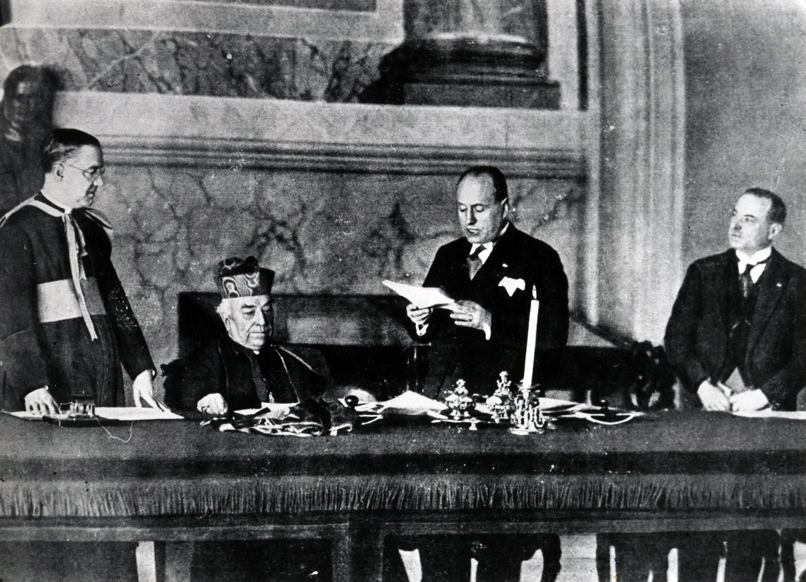 Benito Mussolini mentre legge la bozza degli accordi. Nello specifico si componevano di un Trattato per definire i rapporti tra Stato italiano e Santa Sede a livello di diritto internazionale e di un Concordato relativo ai rapporti tra lo Stato italiano e la religione cattolica