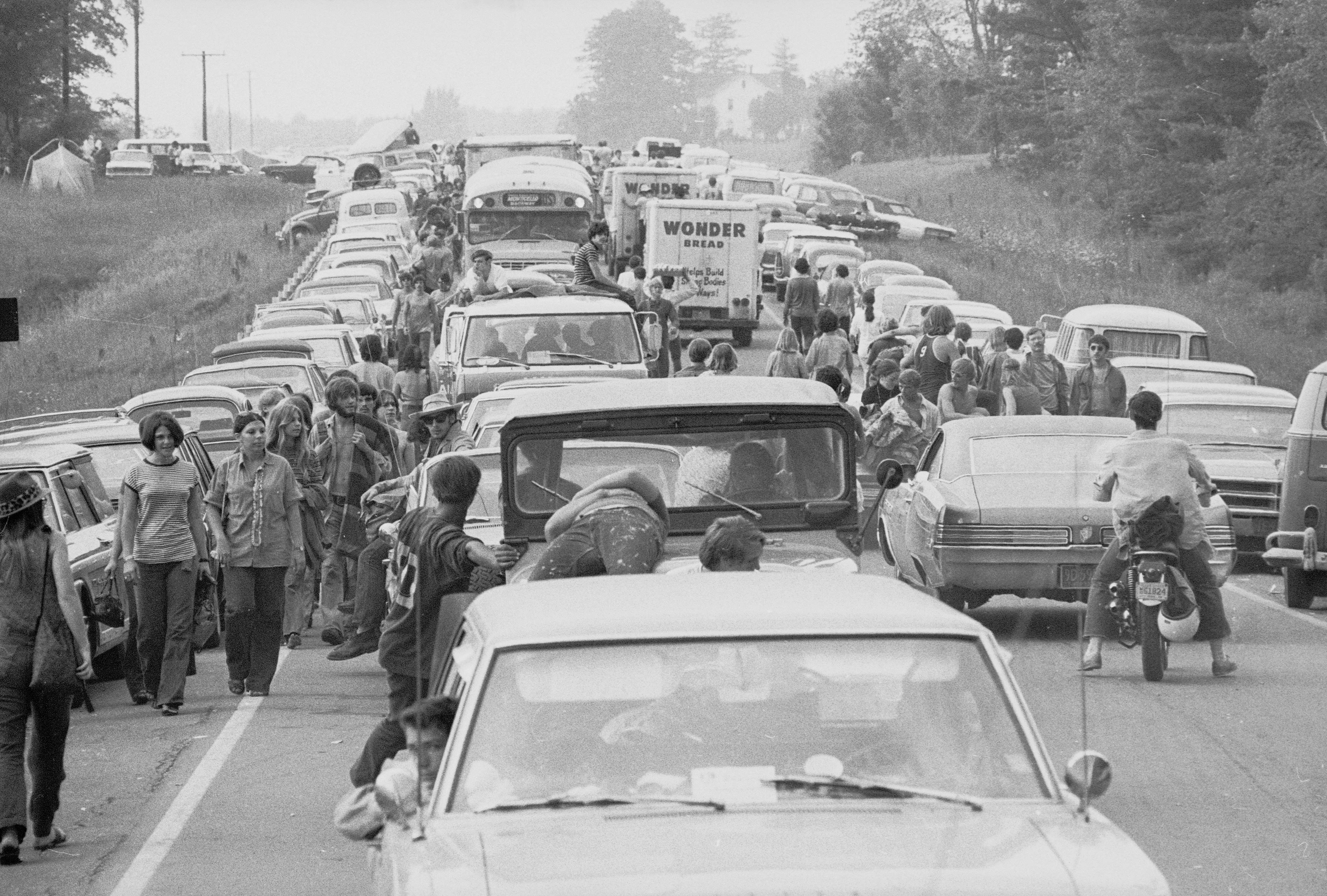 Sulla via di Woodstock. L'affluenza di gente a Bethel, soprattutto ragazzi, fu massiccia e immediata. Il traffico bloccò a lungo alcune autostrade dello stato di New York. I promotori del festival furono Michael Lang, John P. Roberts, Joel Rosenman e Artie Kornfeld. Roberts e Rosenman avevano pubblicato un annuncio sul New York Times e sul Wall Street Journal, presentandosi come 'Challenge International, Ltd.': "Uomini giovani con capitale illimitato cercano interessanti opportunità, legali, di investimento e proposte d'affari". Lang e Kornfeld li contattarono, e con loro progettarono uno studio di registrazione da mettere su nel villaggio di Woodstock, nella contea di Ulster dello stato di New York, un luogo dall'atmosfera ritirata e tranquilla. Presto però immaginarono di realizzare al suo posto un più ambizioso festival musicale e artistico. Roberts era incerto se abbandonare l'iniziativa, consolidando le perdite che vi aveva subito; infine la sua decisione fu di restare nel gruppo e finanziare il Festival. Woodstock era per loro un'iniziativa commerciale, che chiamarono appunto 'Woodstock Ventures', una possibilità di guadagni. Divenne una manifestazione ad ingresso libero quando gli organizzatori si accorsero di stare attirando centinaia di migliaia di persone in più del previsto: circa 186.000 biglietti erano stati acquistati in prevendita.