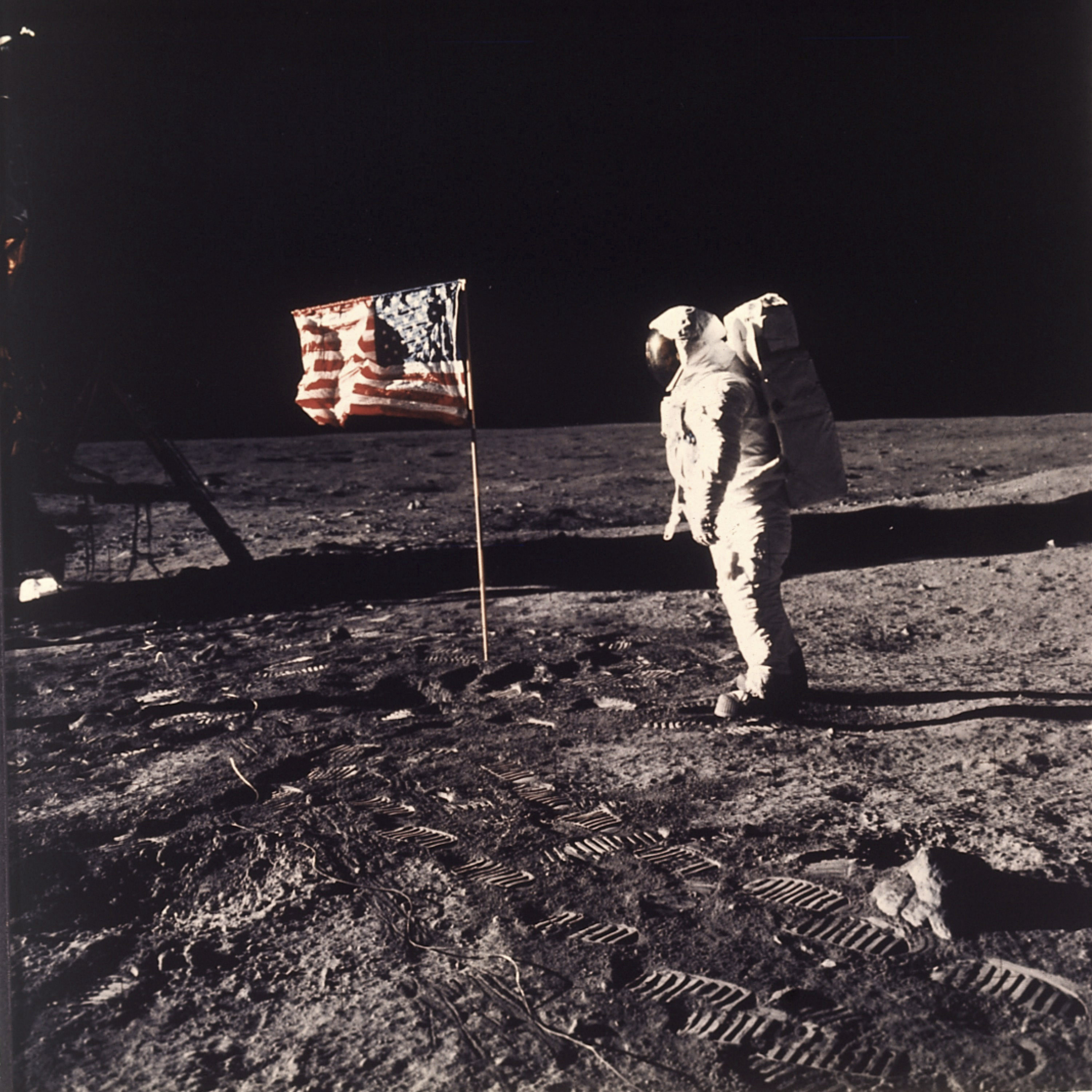 Aldrin vicino alla bandiera americana piantata sulla luna insieme ad una targa che riporta le firme dei tre astronauti e dell’allora presidente americano Richard Nixon e la seguente scritta: “Qui nel luglio 1969 misero per la prima volta piede sulla Luna uomini venuti dal pianeta Terra, siamo venuti in pace per l'intera umanità”