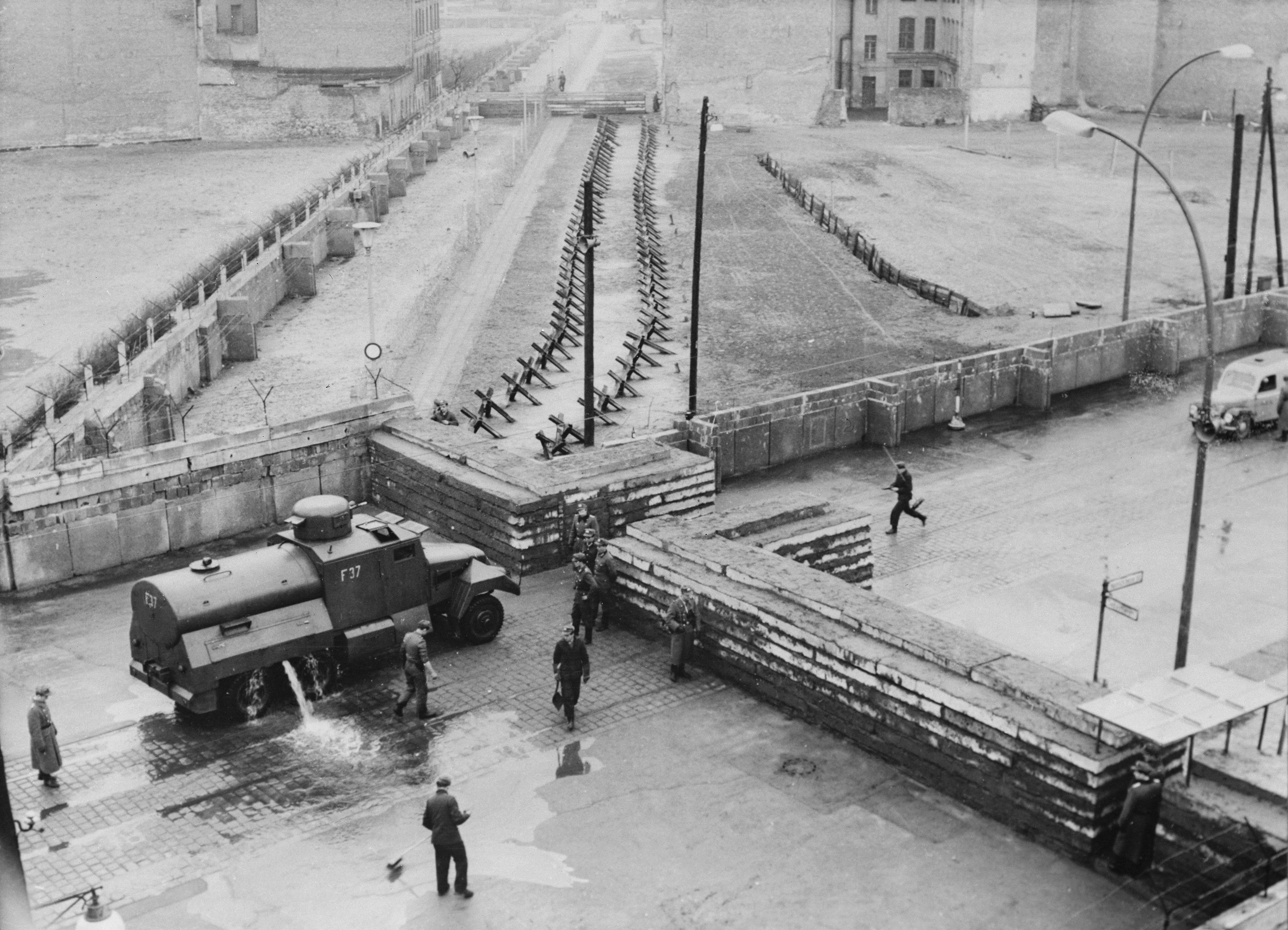 Un camion d’acqua corazzato pulisce la strada dai detriti in un punto di frontiera di Berlino Est, nel dicembre 1961