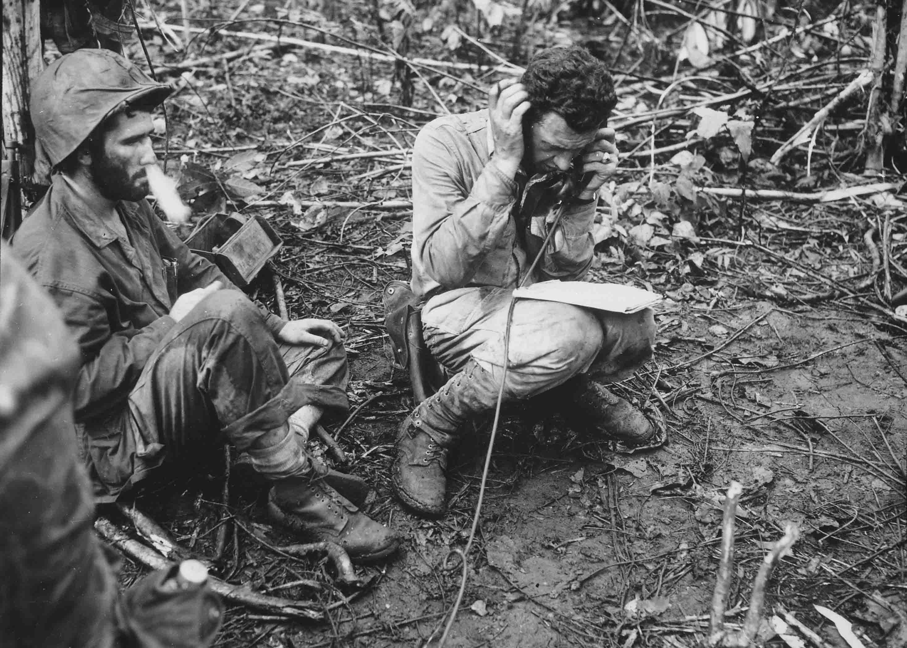 Gennaio 1944. Il tenente colonnello John Weber, seduto sul suo elmetto, riceve un rapporto da uno dei suoi comandanti di compagnia. Il soldato semplice di prima classe Vincent Miley, guardando davanti a sé, fa uscire il fumo di una sigaretta dal naso. Cape Gloucester, Papua Nuova Guinea. Autore sconosciuto. © courtesy Defense Dept. photo (Marine Corps) / Library of Congress