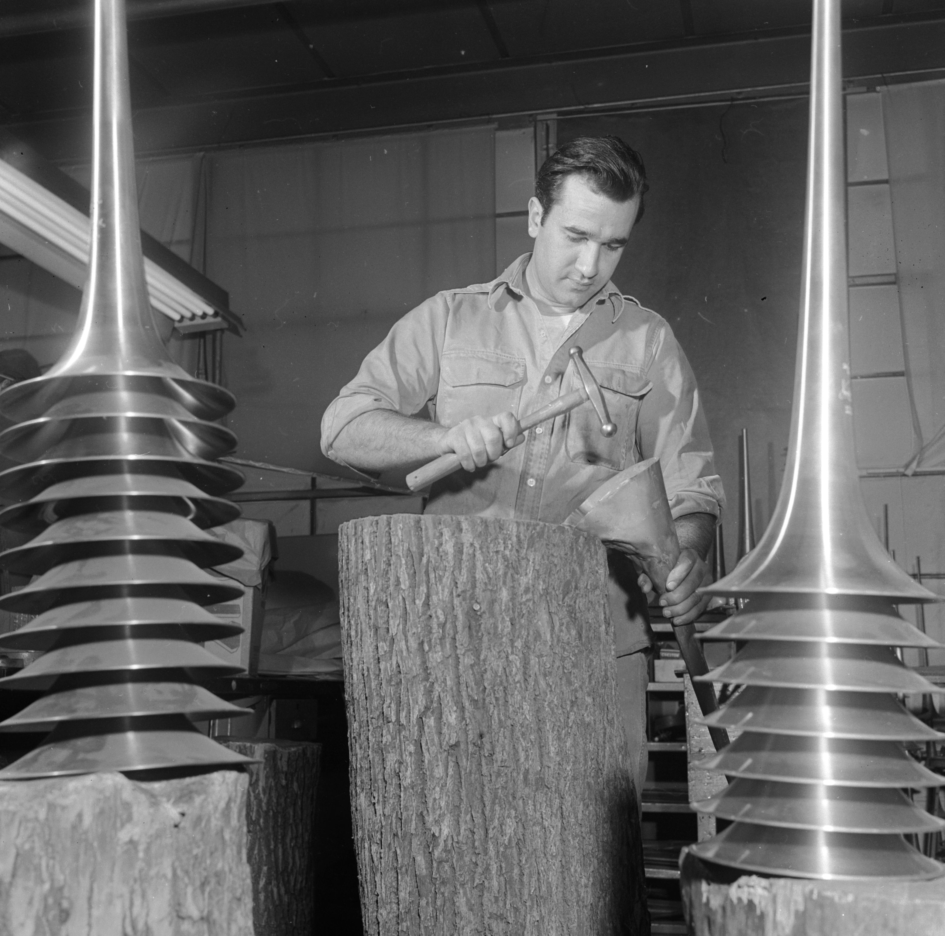 1950: un operaio martella la campana di un trombone in un laboratorio di strumenti musicali negli U.S.A.