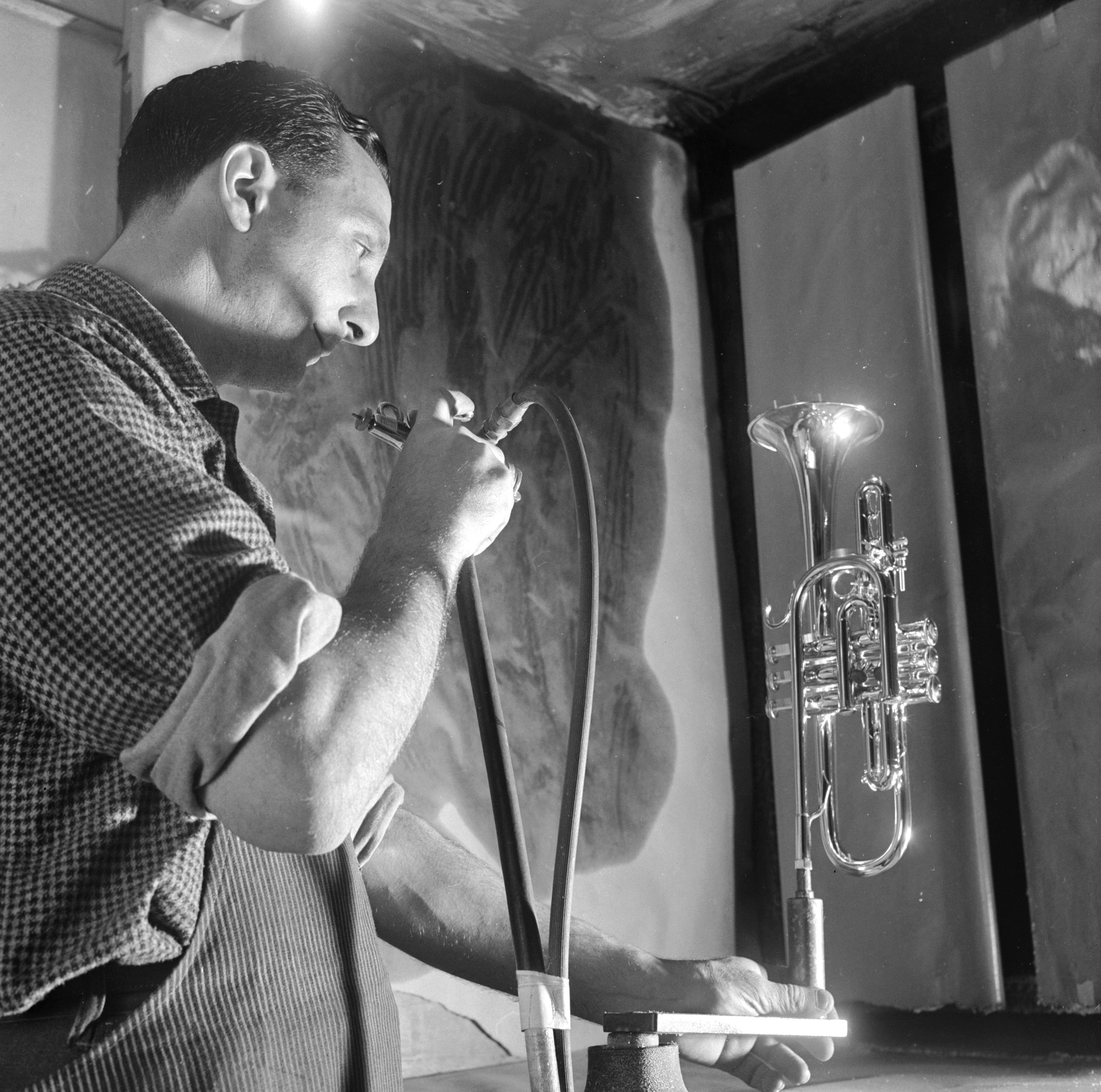 1950: un artigiano soffia la lacca su una cornetta in un laboratorio di strumenti musicali negli U.S.A.