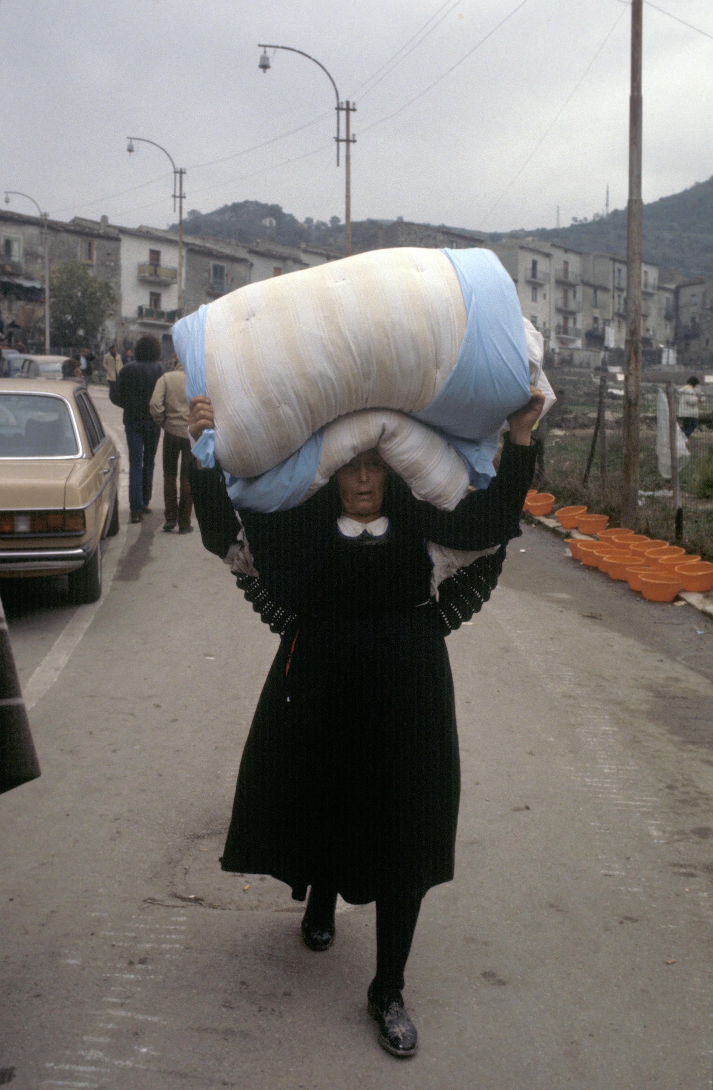 Una sopravvissuta trasporta un materasso recuperato tra le rovine