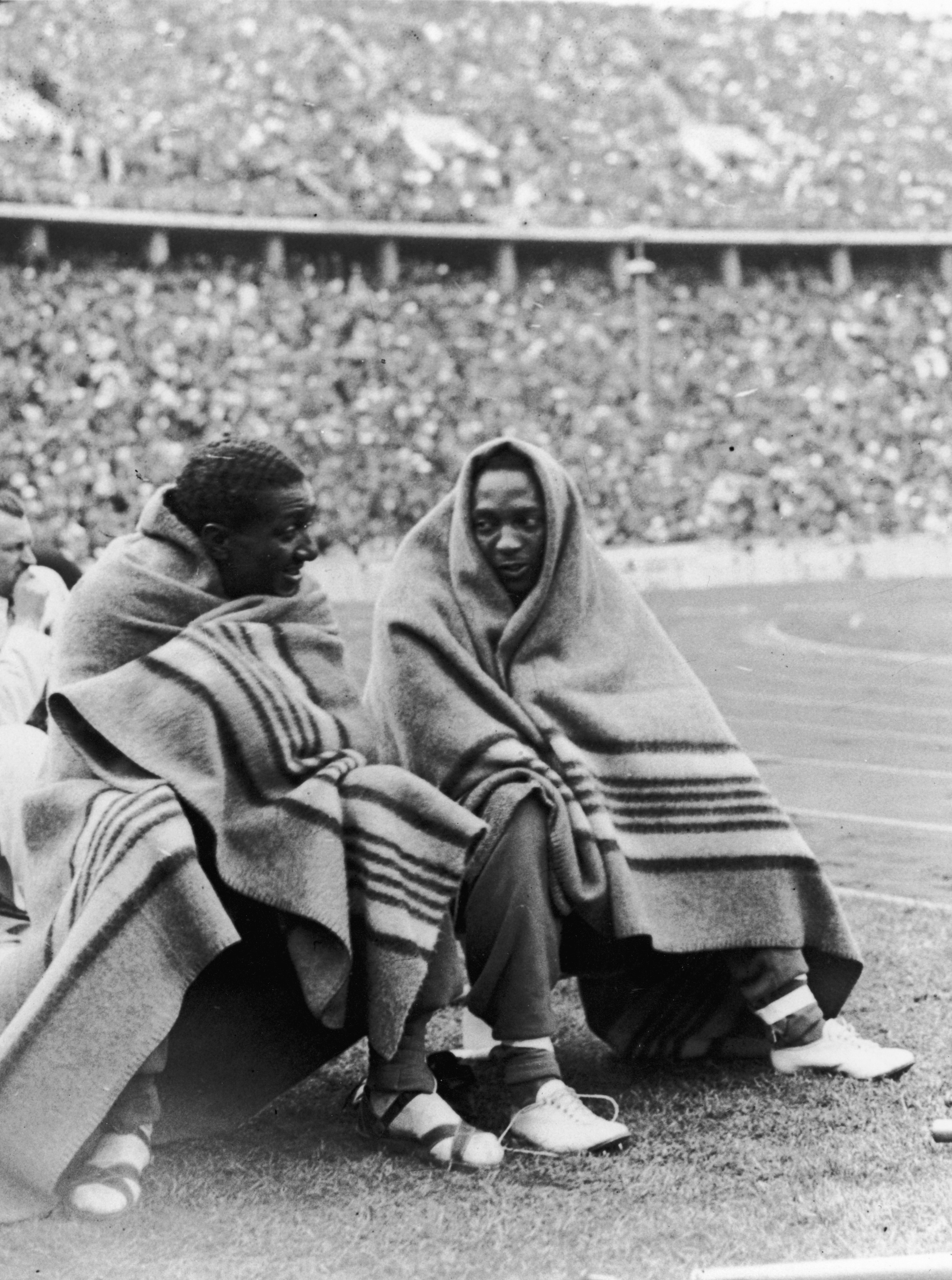Gli atleti americani, Jesse Owens (a destra) e Ralph Metcalf si tengono al caldo sotto le coperte durante le finali dei 100 metri. La coppia ha vinto rispettivamente medaglie d'oro e d'argento.