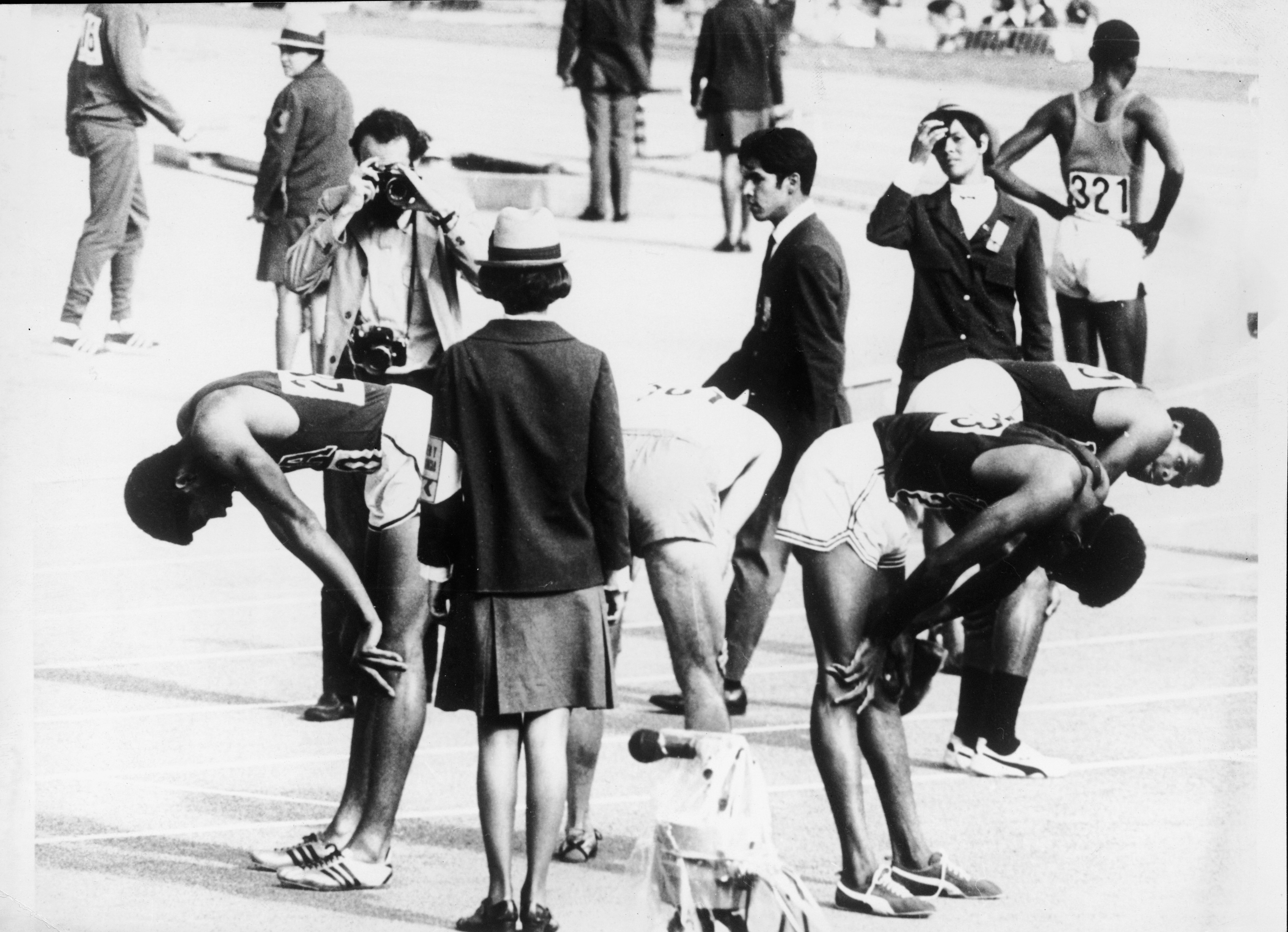  I tre vincitori della medaglia americana nella finale dei 400 metri maschili visti da una prospettiva insolita: piegati tra i giudici di gara per riprendere fiato. Da sinistra, Larry James (medaglia d'argento), un velocista non identificato in bianco, Ronald Freeman (medaglia di bronzo), e Lee Evans, che ha vinto l'evento e ha stabilito il record mondiale