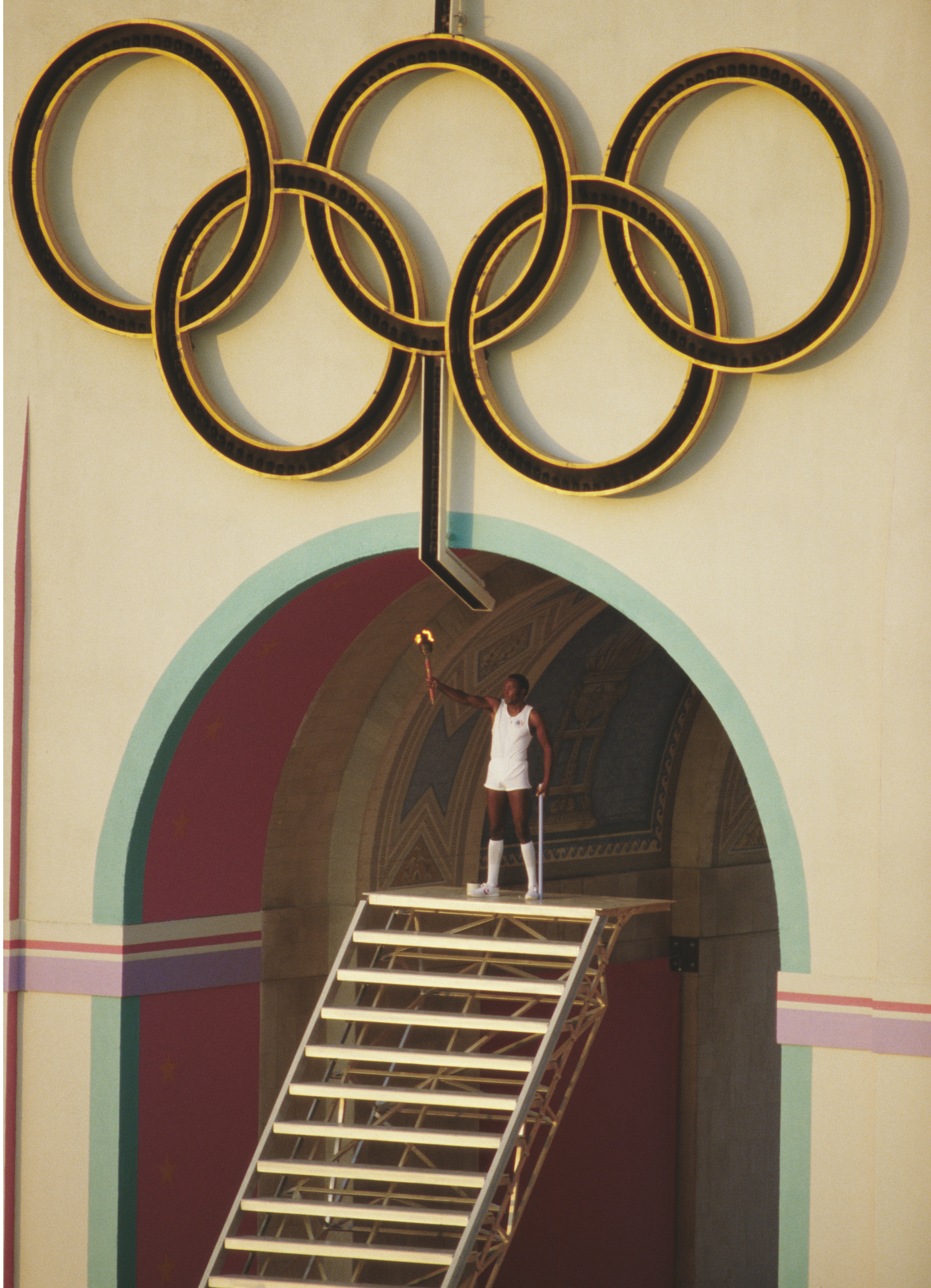 Rafer Johnson, atleta degli Stati Uniti e vincitore del decathlon alle Olimpiadi estive di Roma del 1960 tiene la torcia in alto per accendere la fiamma olimpica durante la cerimonia di apertura a Los Angeles