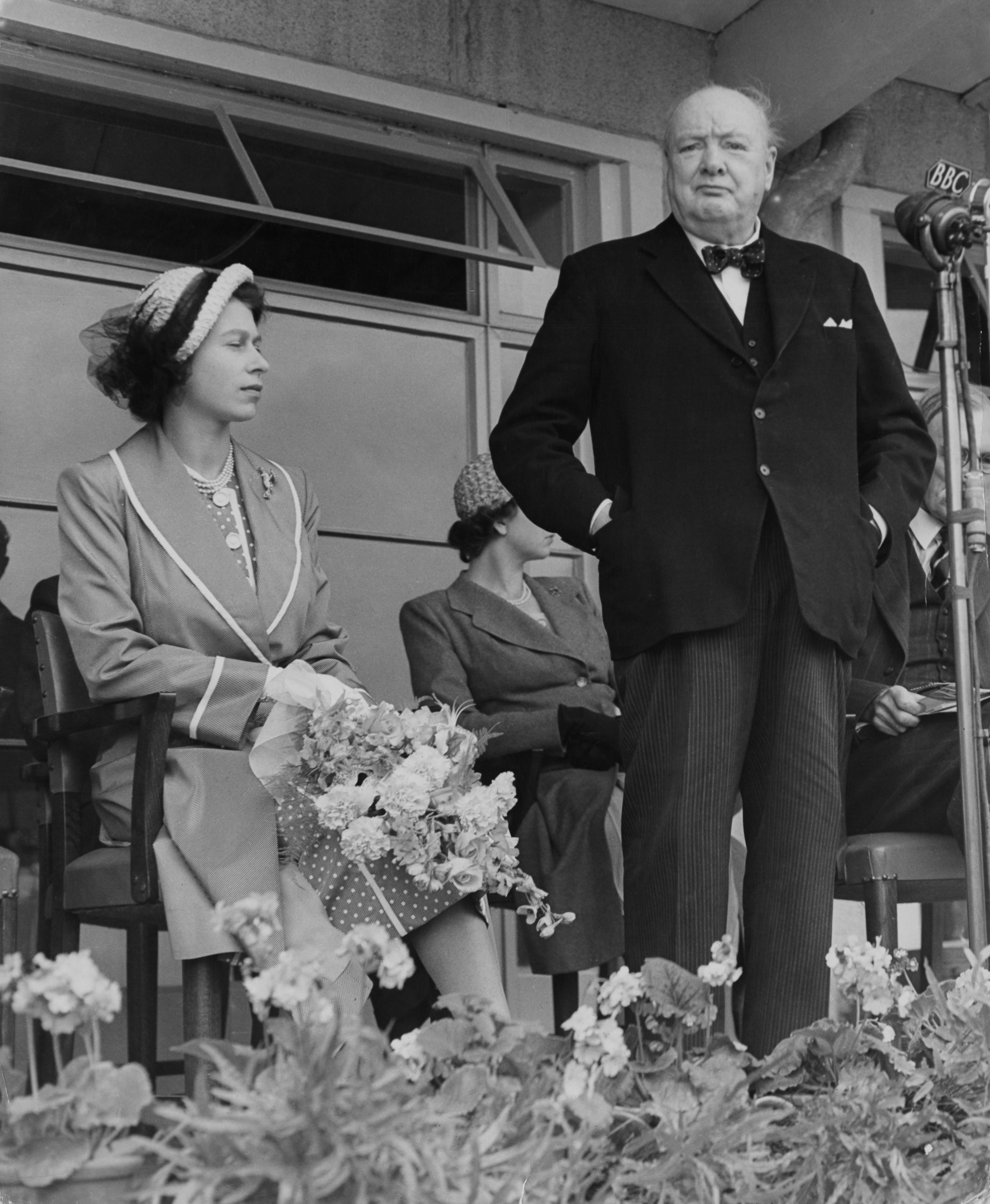 Il Primo Ministro Winston Churchill parla durante una manifestazione pubblica nel 1951, alla presenza della Principessa Elisabetta. E' noto lo stretto legame tra i due, Churchill così definisce la futura Regina a soli due anni: "Che carattere...ha un’aria di autorità e riflessività stupefacente per una bambina"