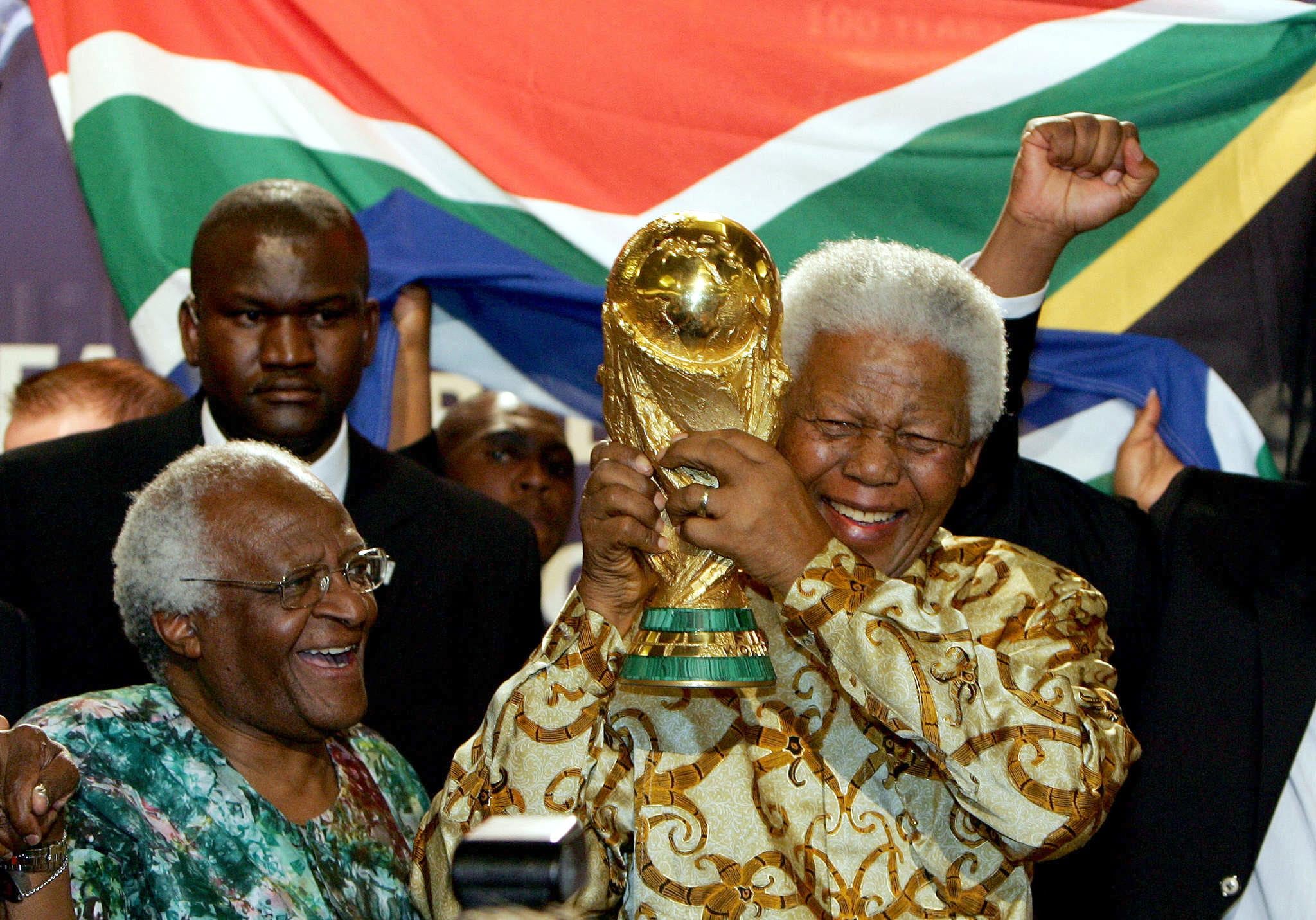 Mandela tiene la Coppa del Mondo di calcio accanto all'arcivescovo Desmond Tutu di Città del Capo, il 15 maggio 2004 presso la sede della Fifa a Zurigo. Il Sudafrica sarà il primo paese africano ad ospitare questo evento grazie al presidente Mandela