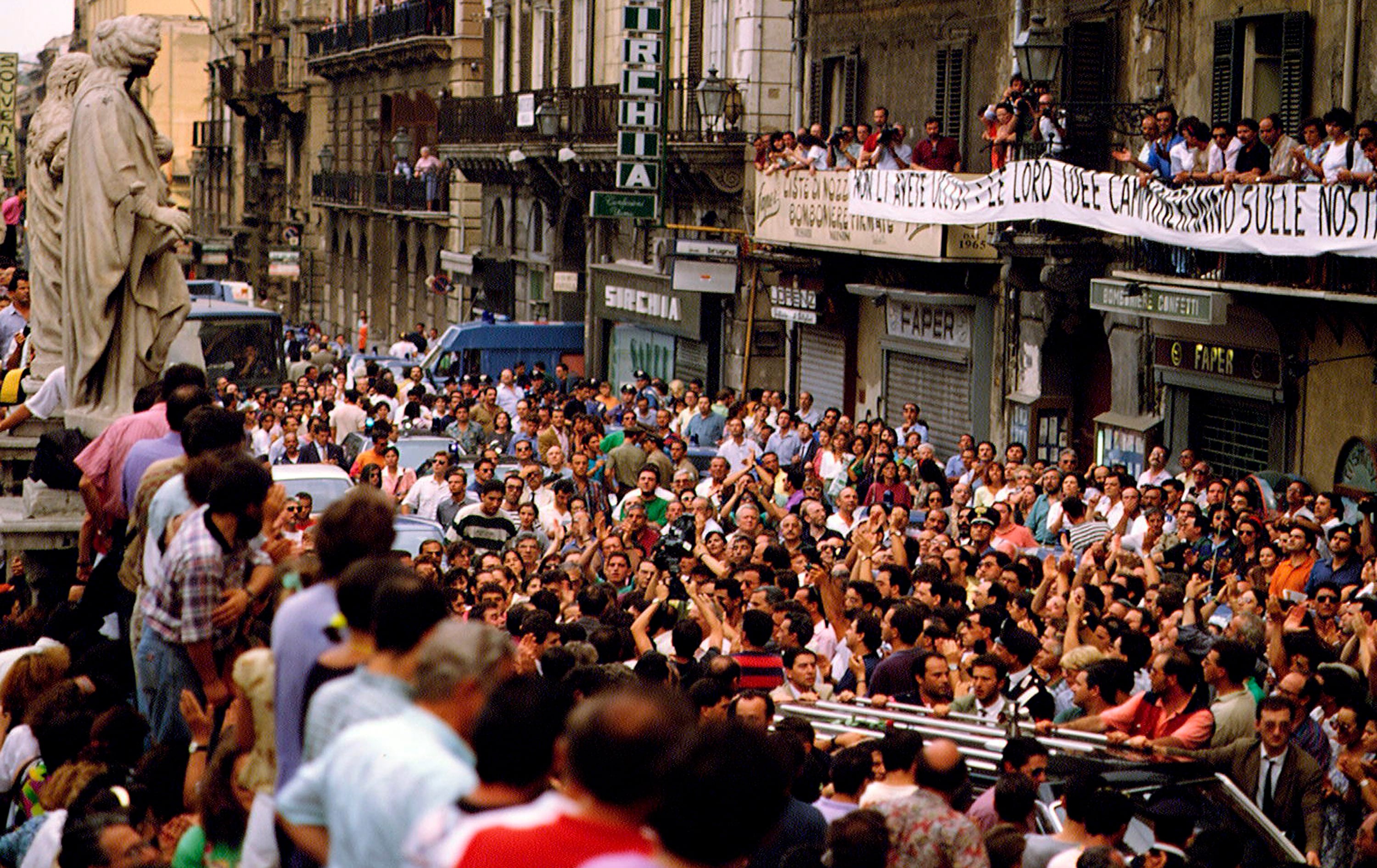 La folla applaude al passaggio delle bare del giudice italiano Paolo Borsellino e della sua scorta di polizia durante i funerali che si sono tenuti nella Cattedrale di Palermo il 24 luglio 1992