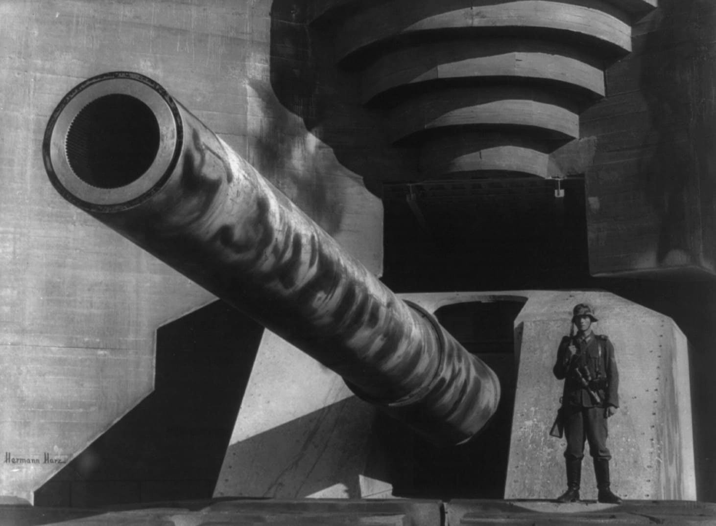 Canna di un grosso cannone con soldato tedesco presso una fortificazione. La foto risale al 1943, ma è proprio contro fortificazioni come queste che la forza d'invasione alleata sta per andare a scontrarsi durante la battaglia di Normandia. 1943, Normandia, Francia. Fotografo: Hermann Harz Per gentile concessione della Library of Congress 