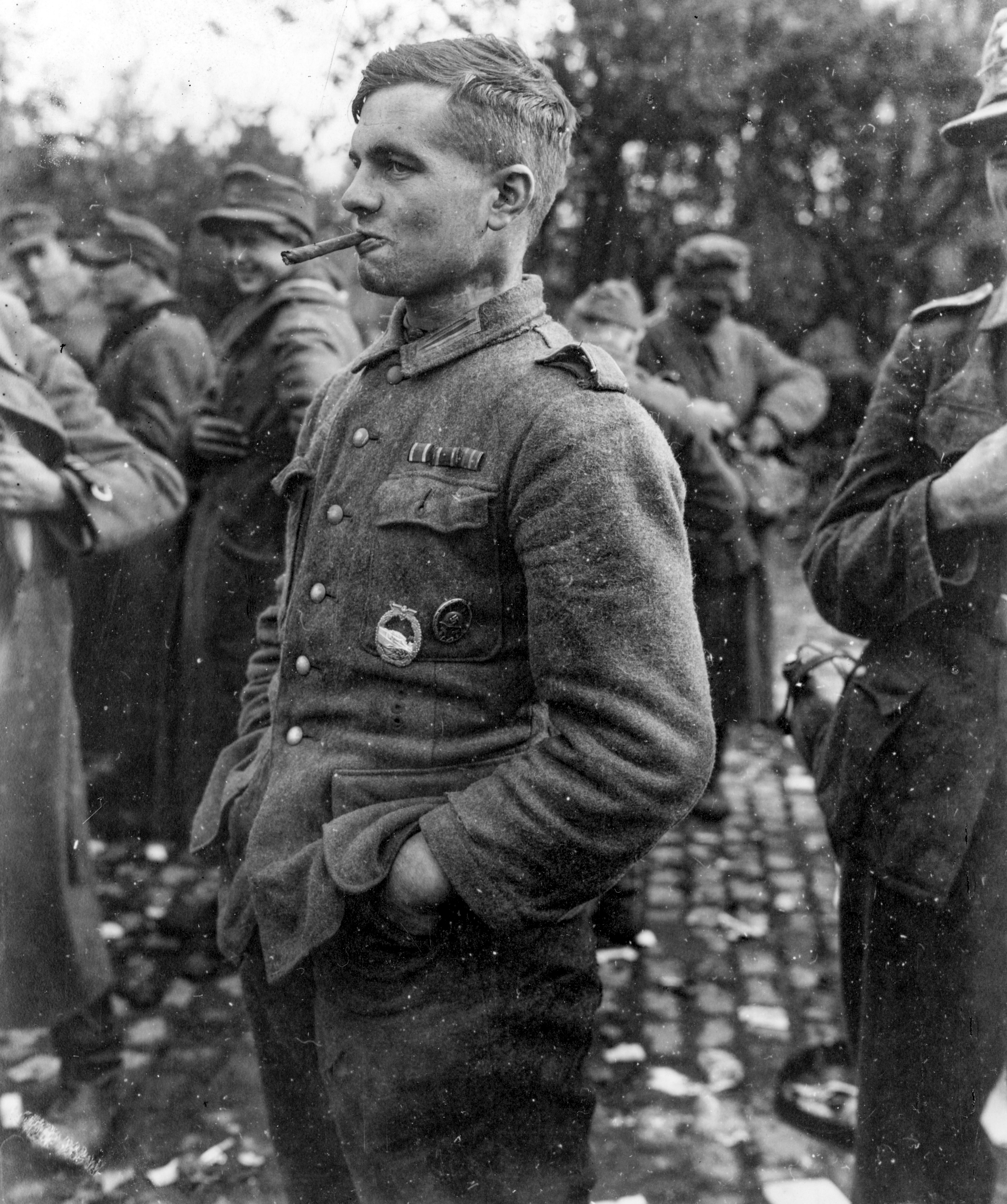 Questo prigioniero di guerra tedesco era uno dei tanti che si è arreso con la cattura di Aquisgrana, in Germania. Qui fuma un sigaro mentre mostra con orgoglio una medaglia da torpediniere vinta come ex marinaio della Marina nazista. 21 ottobre 1944, Aquisgrana, Germania. Fotografia di Signal Photo Digitalizzato da Signal Corps Archive Per gentile concessione degli U.S. National Archives 