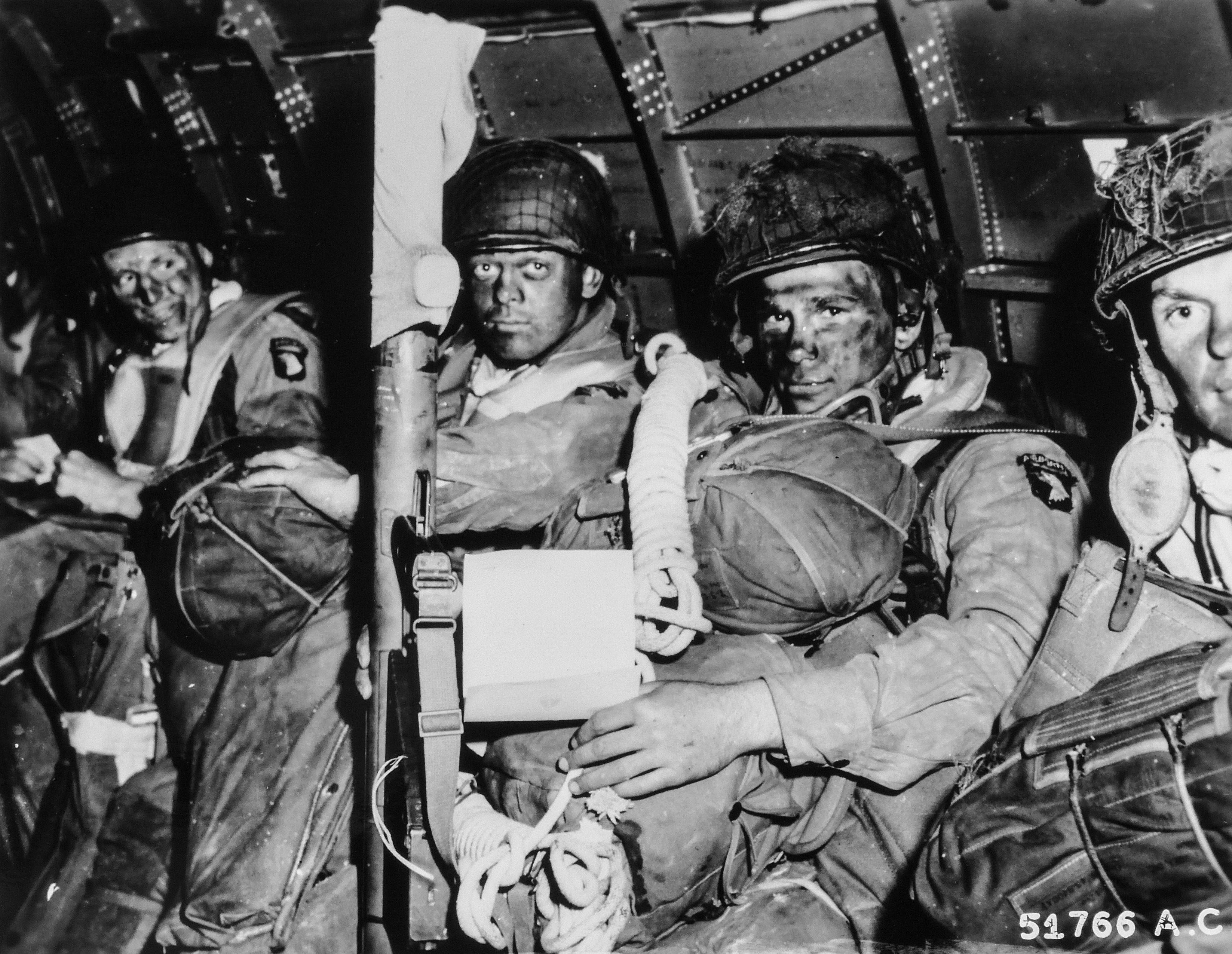 Volti risoluti di paracadutisti poco prima di decollare per l'assalto iniziale del D-Day. Il paracadutista in primo piano ha appena letto il messaggio di buona fortuna del Gen. Eisenhower e stringe il suo bazooka con determinazione. Nota l'ordine di Eisenhower per il D-Day nelle mani del paracadutista in primo piano. 6 giugno 1944, Inghilterra. Fotografo: sconosciuto o non fornito Per gentile concessione degli U.S. National Archives 